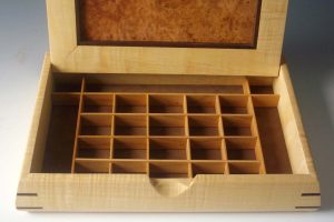Mens jewelry box made of exotic woods that is shown open to reveal cubed compartments for jewelry