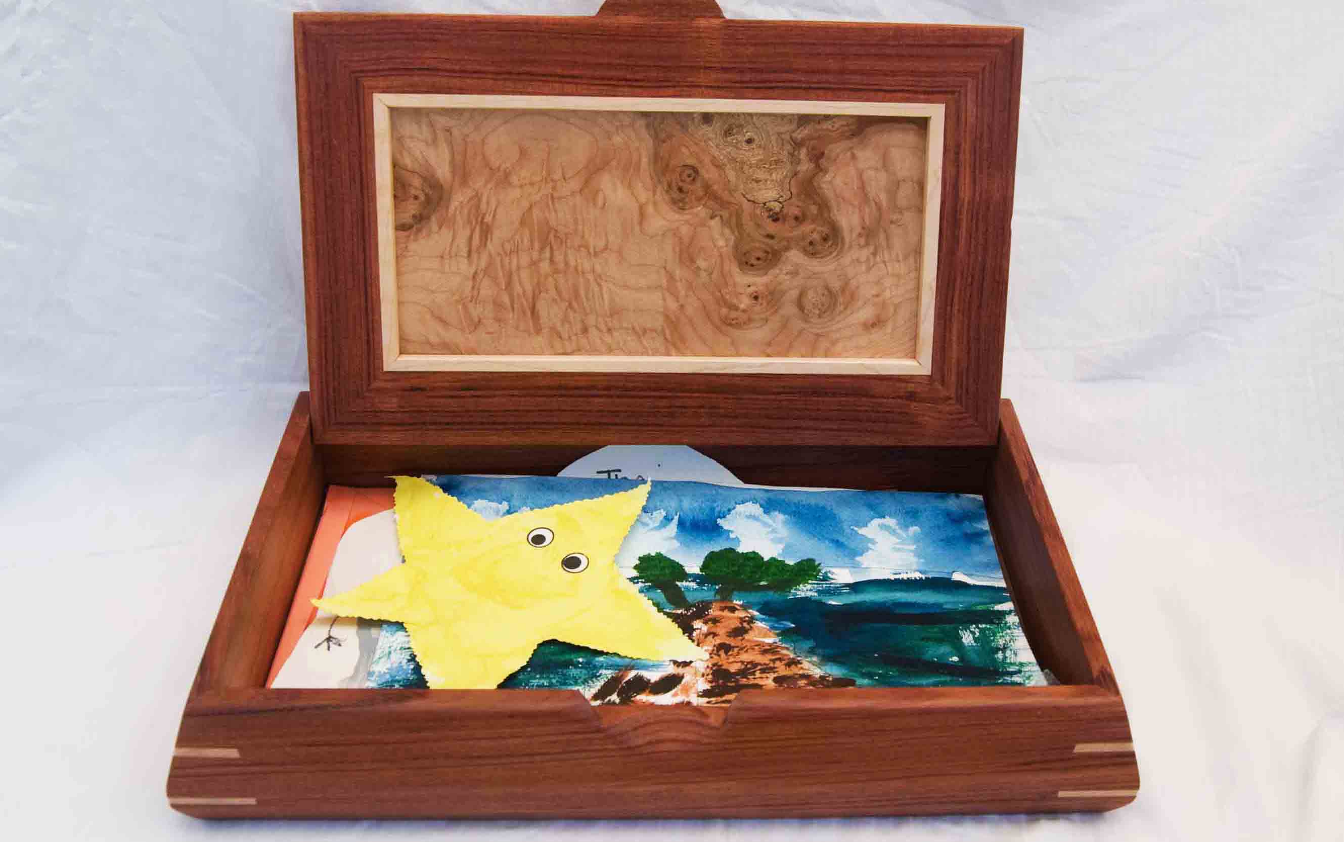 A handmade decorative wooden box is shown open and inside it holds kids art and paintings